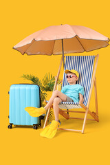 Cute little boy in flippers with glass of cocktail sitting in deck chair and suitcase on yellow background. Travel concept © Pixel-Shot