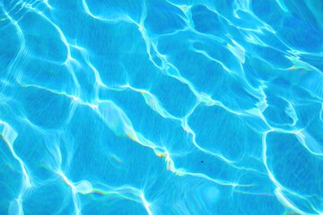 Close-up view of clear blue water surface with sunlight reflections creating ripples and shimmering patterns