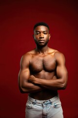 Fototapeta premium Strong confident shirtless man with crossed arms standing against a dark red background with serious expression