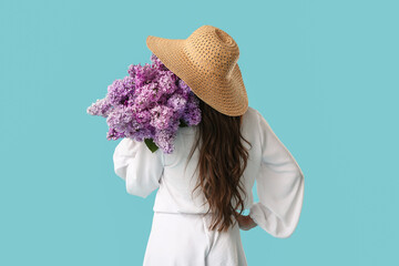 Young woman with bouquet of blooming lilac flowers on blue background, back view