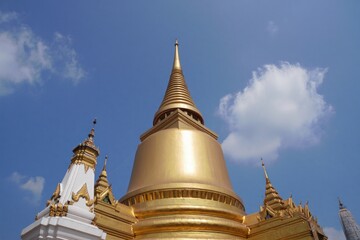 Naklejka premium Ornate golden Buddhist stupa and surrounding intricately decorated structures set against a bright blue sky with white clouds