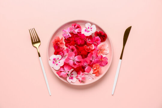 Plate with beautiful edible flowers and cutlery on pink background