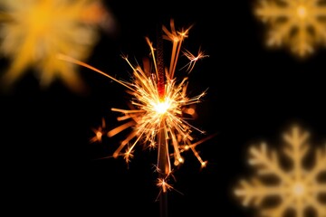 Fototapeta premium Bright golden sparkler glowing against a black background with blurred golden snowflake shapes creating a festive warm atmosphere