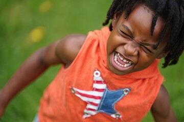 Young child outdoors with eyes closed, yelling or expressing strong emotion, wearing an orange sleeveless top with a star design, in a green grassy area