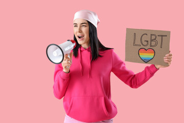 Beautiful young woman holding placard with word LGBT and megaphone on pink background