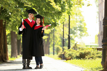 Couple of happy graduating students with diplomas hugging outdoors