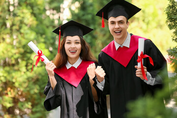 Couple of happy graduating students with diplomas outdoors