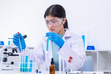 Fototapeta premium A young Asian female scientist in lab coat and gloves holds a glass pipette carefully in a science laboratory, demonstrating scientist, experiment, research, and laboratory skills.