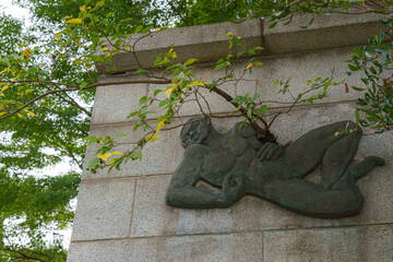 Tokyo, Japan - Sep 30 2024, close-up view of a wall with a metal bas-relief in the form of a reclining man, from which a tree grows, in the cemetery at Gotokuji Temple, without people, Tokyo, Japan
