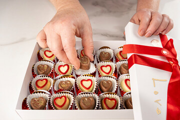 Woman taking an assorted chocolate from a white box.