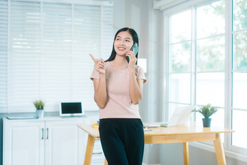 Asian housewife relaxes at a table, using her smartphone for calls, chatting with friends, working...