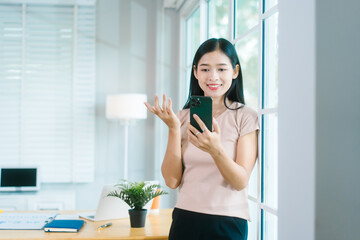Asian housewife relaxes at a table, using her smartphone for calls, chatting with friends, working...