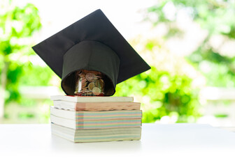 A graduation cap sits on top of a coin jar, which is placed on a stack of books.