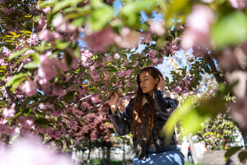 Sakura Blossom Girl: Woman poses in Spring under cherry trees in park for picture in daylight.