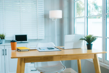.A clean, modern home office features a laptop, plant, and organized desk, ready for productive work in a bright, minimalist setting.