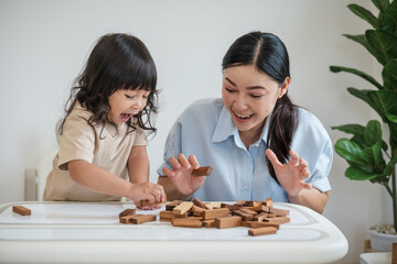 toddler girl with mother playing wooden block toy together and shocked with tower collapses