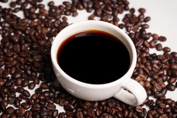 Freshly brewed black coffee in a white cup beside roasted beans on rustic table, capturing morning aroma, warmth, and cozy atmosphere.