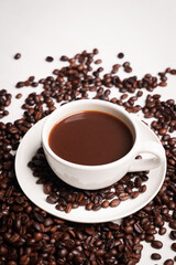 Freshly brewed black coffee in a white cup beside roasted beans on rustic table, capturing morning aroma, warmth, and cozy atmosphere.