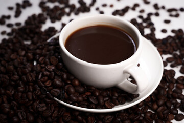 Freshly brewed black coffee in a white cup beside roasted beans on rustic table, capturing morning aroma, warmth, and cozy atmosphere.