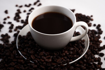 Freshly brewed black coffee in a white cup beside roasted beans on rustic table, capturing morning aroma, warmth, and cozy atmosphere.