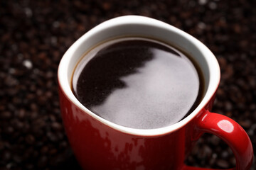 Freshly brewed black coffee in a white cup beside roasted beans on rustic table, capturing morning aroma, warmth, and cozy atmosphere.