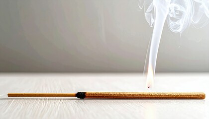 Burning Incense Stick With Smoke and Glowing Ember on Wooden Surface Against Neutral Backdrop