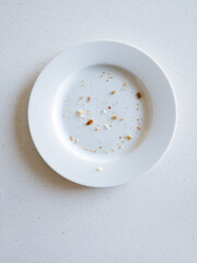 Crumbs on an empty white round plate placed on a white surface.
