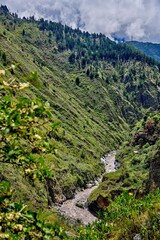 Lush green valley with a winding river flowing through rocky terrain, surrounded by towering mountains and dramatic clouds, showcasing the beauty of nature a serene landscape in Ecuador.Latin America
