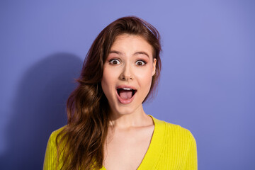 Excited young woman in casual yellow sweater against a purple backdrop expressing astonishment and surprise