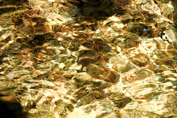 Close-up abstract of sunlight reflecting on rippled clear water revealing a golden-hued riverbed at Qing Shan Waterfall, Taiwan.