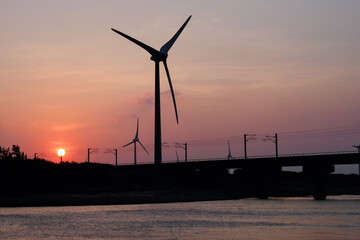 Silhouette of wind turbines and a bridge over water at sunset, captured on October 7, 2012, in Miaoli County, Taiwan.