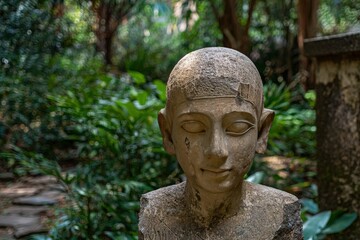 Obraz premium Ancient Egyptian bust statue in a lush garden setting.