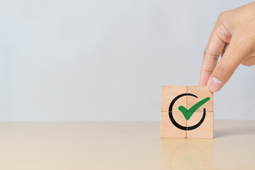 Tick mark icon on cube block being assembled by hand. Symbol of project approval, certified documents, and quality control process