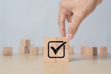 Hand placing tick sign on wooden block cube. Document approval, business project validation, and quality assurance concept