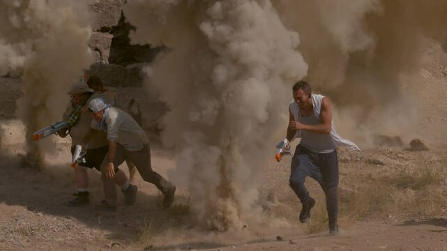 Group with bright toy guns running away as dust explosions go off around them, slow motion shot