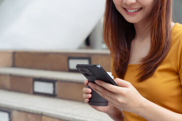 Woman holding smartphone with coffee cup while walking in the urban city.