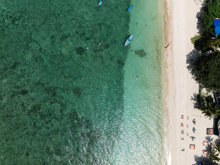 Crystal-clear turquoise water near a sandy shore with small anchored boats. Thailand, Koh Tao.
