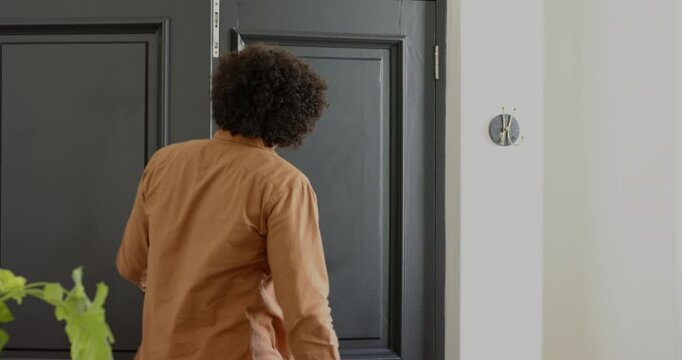 Man in foyer spotting friends outside, opening front door, hugging visitor and gesturing him inside