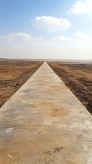 Long straight concrete pathway extending through arid landscape with distant horizon under blue sky and scattered clouds for travel or transportation themes