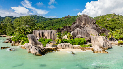 Granite rocks and dense greenery meeting the turquoise ocean on a sunny day. Anse Source d'Argent. Seychelles, La Digue.