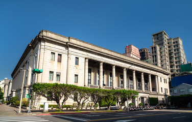 The neoclassical Bank of Taiwan headquarters stands on a sunny street corner in Taipei's Zhongzheng District, its tall granite colonnade and symmetrical stone facade contrasting with nearby modern