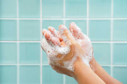 Man washing hands with soap with white foam against mint tiles background in bathroom side view close-up.