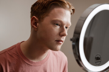 Man Looking into Vanity Mirror Preparing for Skincare Routine
A young man looks thoughtfully into a...