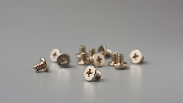 close-up of small silver colored screws scattered on gray textured background surface, machine screws with flat phillips head drive, soft focus with copy space