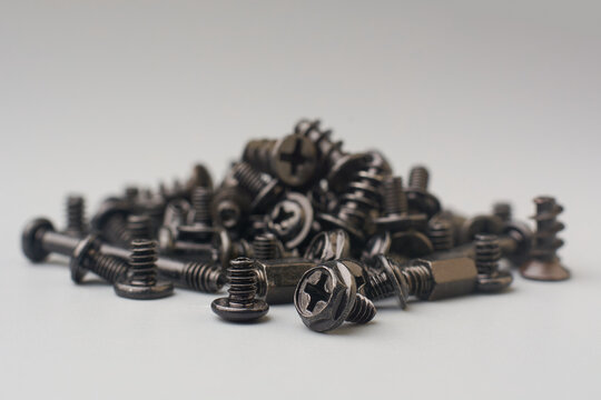 pile of various dark colored screws scattered on gray textured background surface, computer fasteners with flat and pan phillips head drive, soft focus with copy space - Powered by Adobe