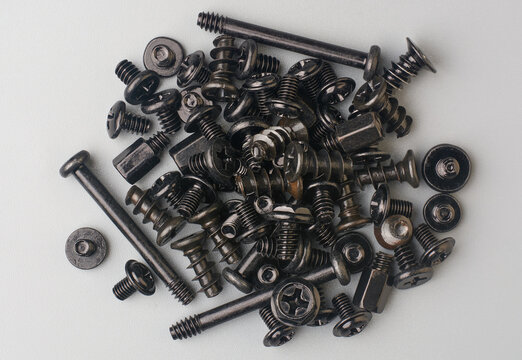 pile of various dark colored screws scattered on gray textured background surface, computer fasteners with flat and pan phillips head drive, taken straight from above - Powered by Adobe