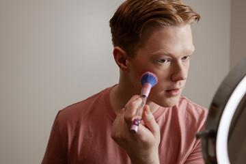 A Close-up of A Young Man Applying Blush In Front Of A Ring Light Mirror
Young man applying makeup...