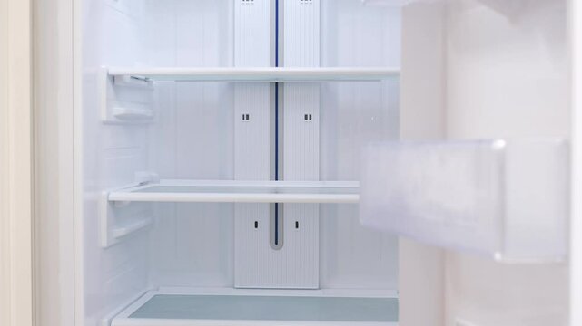 Modern white open refrigerator close-up with empty shelves, front view.