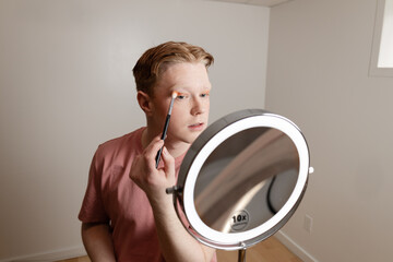 A Medium Shot of A Young Man Applying Eyeshadow in Front of Mirror
Close-up of a young man applying eyeshadow with a blending brush while looking into a vanity mirror with LED lighting. 