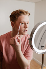 A Vertical Medium Shot of A Man Applying Eyeshadow Makeup Routine in Front of Mirror
A young man...